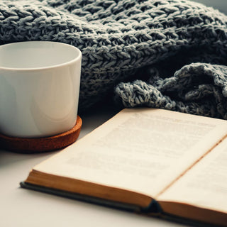 An open book next to a white mug and a grey waffle throw