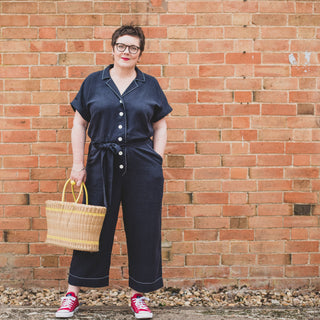 Female wearing Cressida Jumpsuit Sewing Pattern in navy fabric standing in front of a  brick wall
